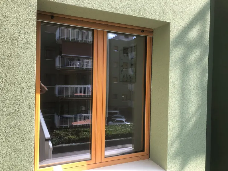 Finestra a due ante con telaio color legno, vista dall'esterno su una parete verde